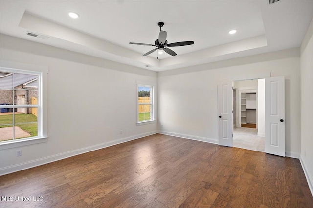 empty room with ceiling fan, dark hardwood / wood-style floors, and a raised ceiling