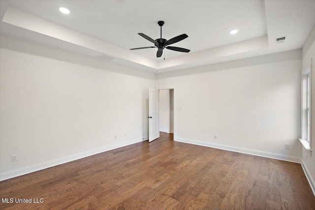 unfurnished room with a tray ceiling, dark wood-type flooring, and ceiling fan