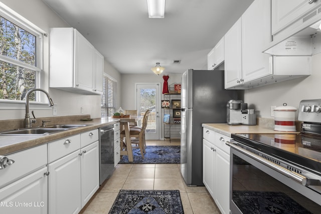 kitchen with custom range hood, a sink, appliances with stainless steel finishes, white cabinets, and light tile patterned flooring