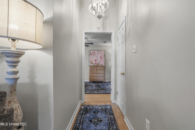 hallway with a notable chandelier, light wood-style flooring, and baseboards