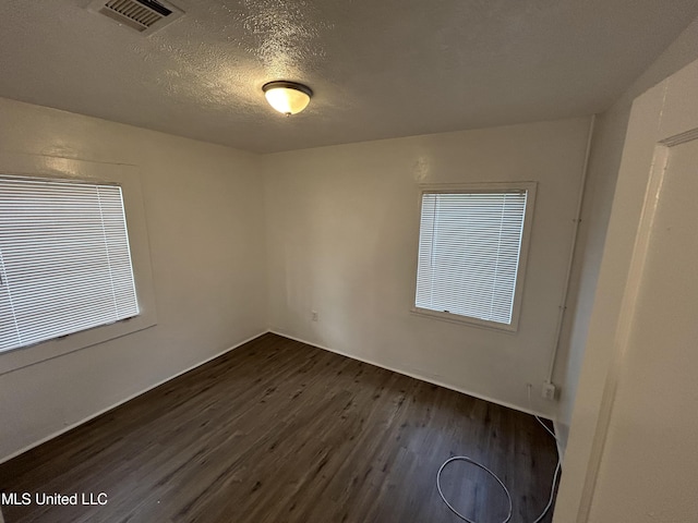 empty room featuring dark wood-style flooring, visible vents, and a textured ceiling