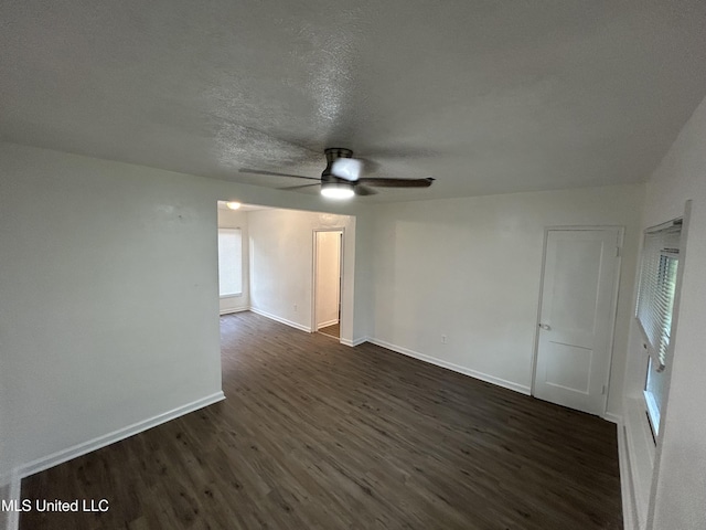 spare room featuring dark wood-type flooring, a textured ceiling, ceiling fan, and baseboards