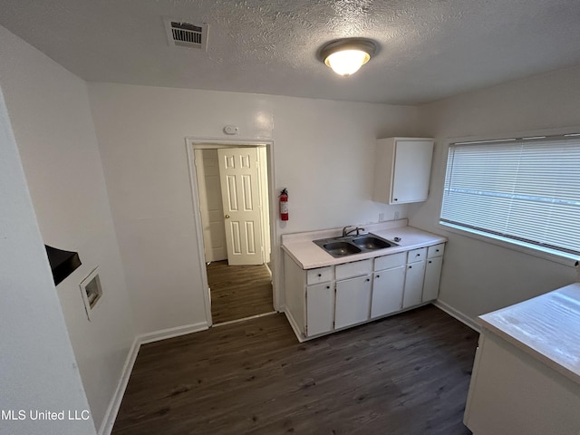 kitchen with visible vents, white cabinets, a sink, light countertops, and dark wood-style floors