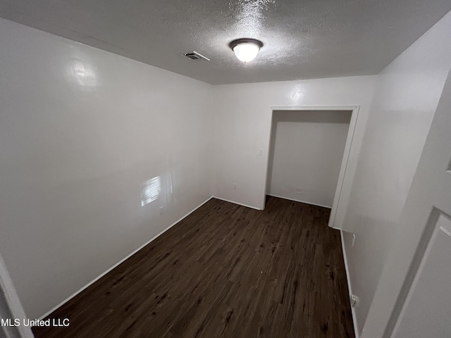 unfurnished bedroom with a textured ceiling, dark wood finished floors, and visible vents