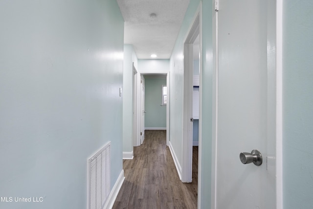 hallway with a textured ceiling, wood finished floors, visible vents, and baseboards