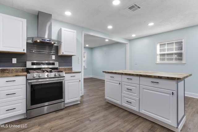 kitchen featuring wall chimney range hood, stainless steel gas range oven, visible vents, and white cabinets