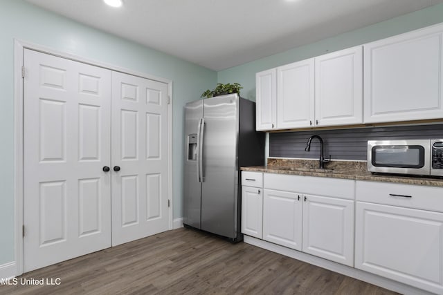 kitchen with a sink, white cabinets, appliances with stainless steel finishes, dark stone counters, and dark wood finished floors