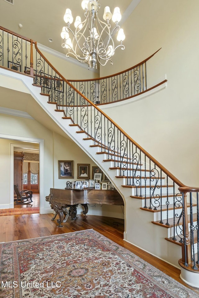 stairway featuring visible vents, a high ceiling, ornamental molding, wood finished floors, and baseboards