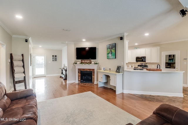 living room featuring a tiled fireplace, crown molding, and light wood-type flooring