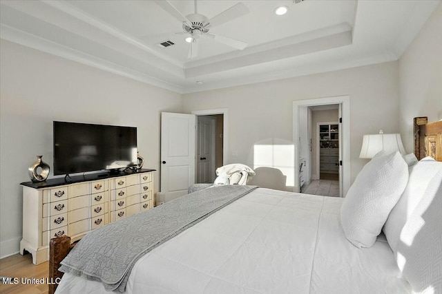 bedroom with hardwood / wood-style floors, ceiling fan, ensuite bath, and a tray ceiling