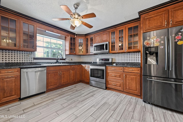 kitchen with brown cabinets, decorative backsplash, a sink, appliances with stainless steel finishes, and glass insert cabinets