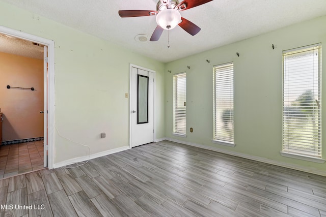 empty room featuring a textured ceiling, wood finished floors, baseboards, and ceiling fan