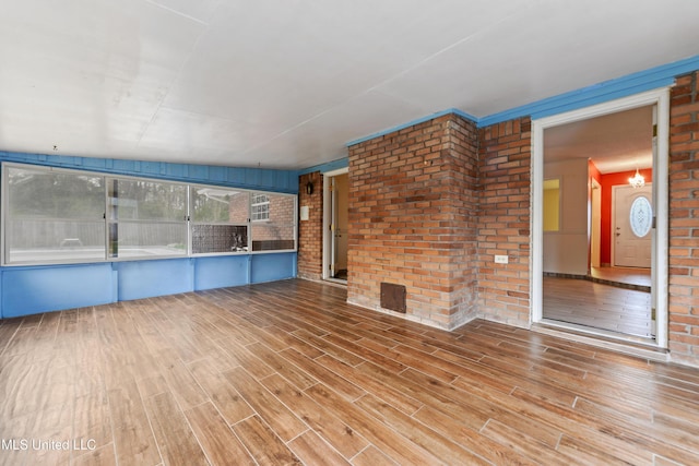 unfurnished living room featuring wood finished floors and brick wall