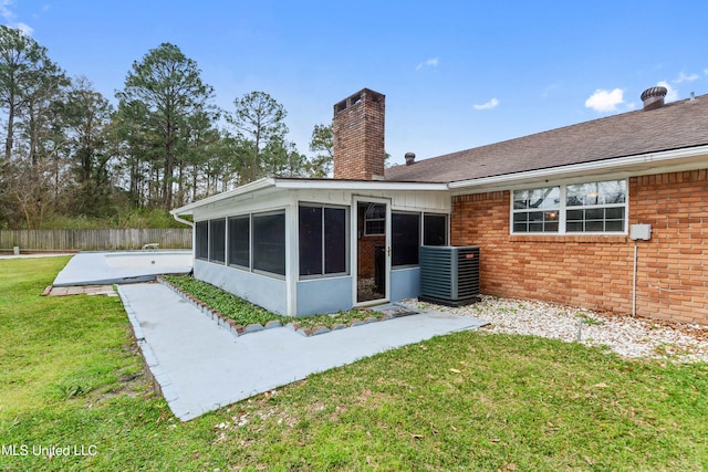 rear view of property featuring brick siding, a lawn, a chimney, and a sunroom