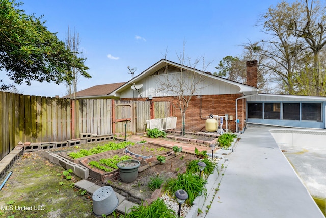 back of property with a garden, a fenced backyard, a sunroom, a chimney, and brick siding