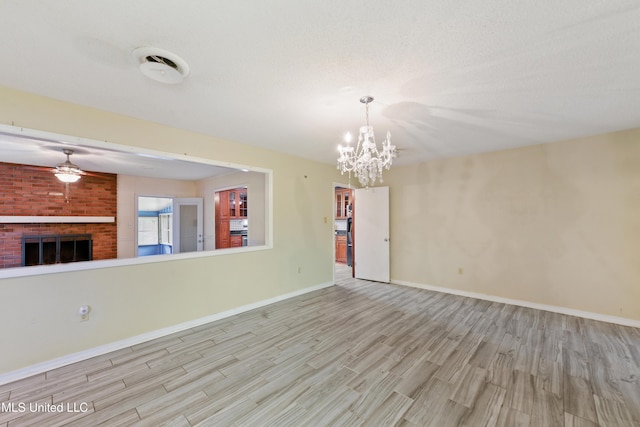 unfurnished living room with wood finished floors, baseboards, visible vents, a fireplace, and ceiling fan with notable chandelier