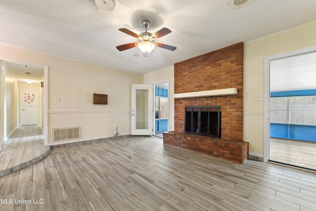 unfurnished living room with visible vents, a textured ceiling, wood finished floors, a brick fireplace, and ceiling fan