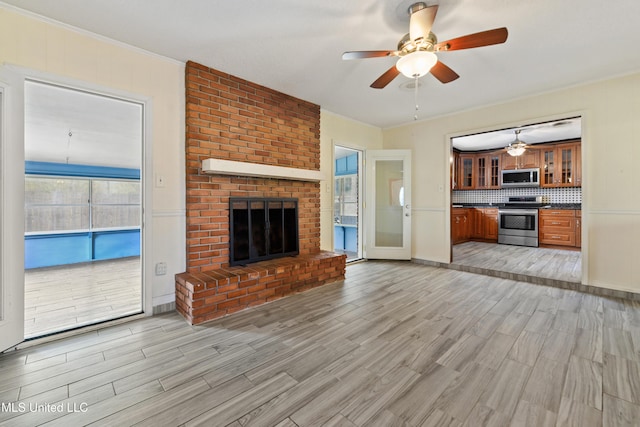 unfurnished living room with light wood finished floors, a brick fireplace, a ceiling fan, and ornamental molding