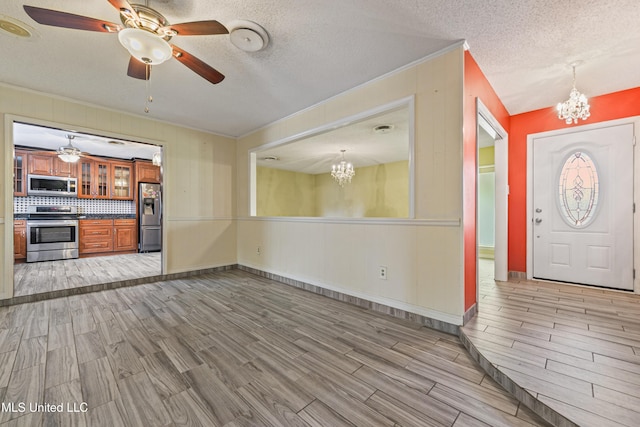 interior space featuring wood finish floors, a textured ceiling, crown molding, and ceiling fan with notable chandelier