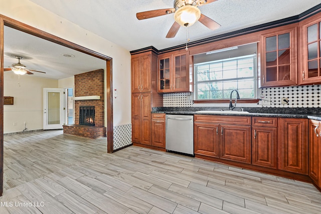 kitchen featuring backsplash, a brick fireplace, ceiling fan, stainless steel dishwasher, and a sink