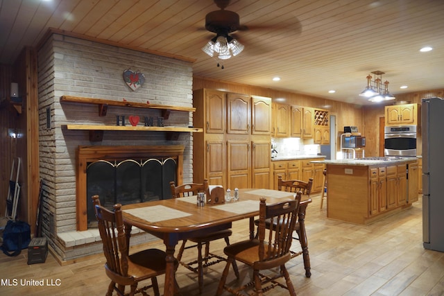 dining space featuring ceiling fan, wooden ceiling, a brick fireplace, wood walls, and light wood-type flooring