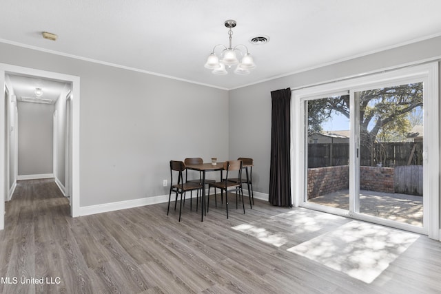 dining room with baseboards, visible vents, ornamental molding, wood finished floors, and a notable chandelier