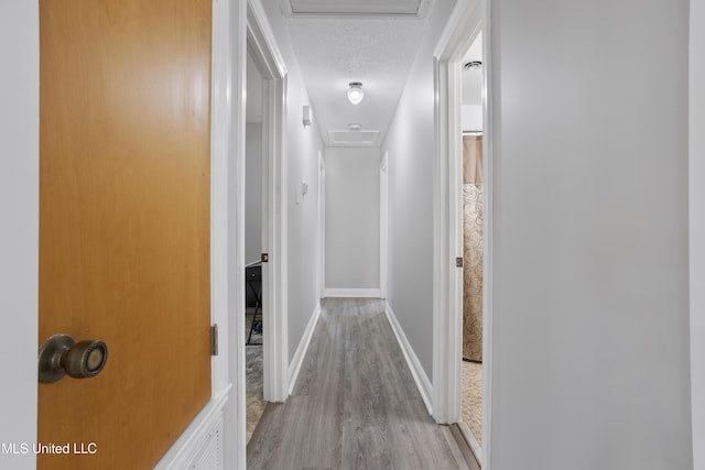 hallway featuring attic access, a textured ceiling, baseboards, and wood finished floors