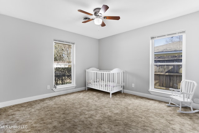 unfurnished bedroom featuring ceiling fan, a crib, carpet, and baseboards