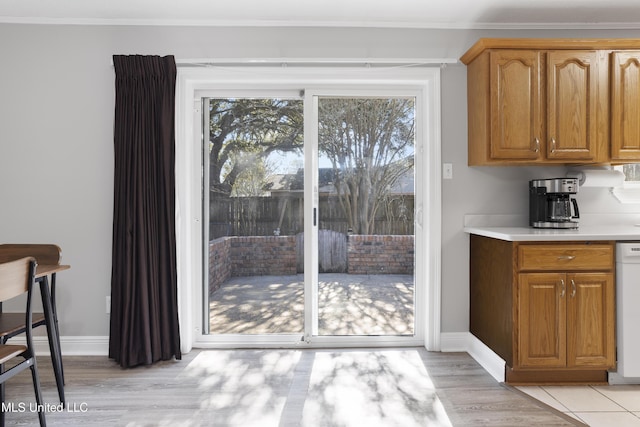 doorway with ornamental molding, light wood-style floors, and baseboards