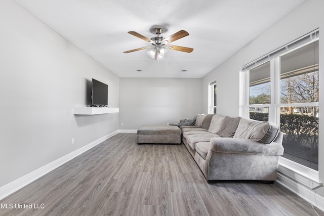 living area with a ceiling fan, baseboards, and wood finished floors