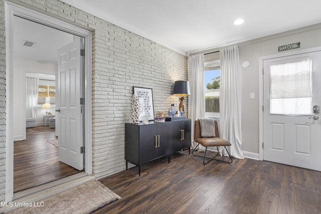 foyer entrance featuring visible vents, baseboards, wood finished floors, and brick wall