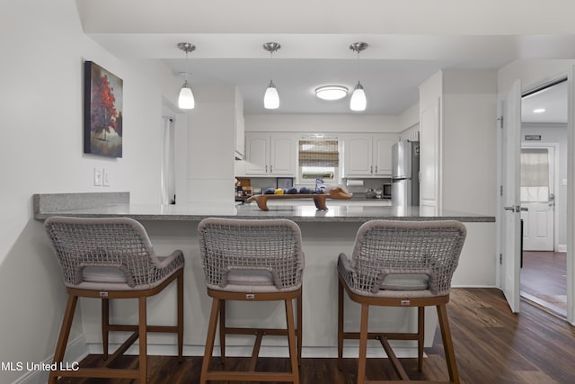 kitchen featuring freestanding refrigerator, white cabinetry, a peninsula, a kitchen bar, and pendant lighting
