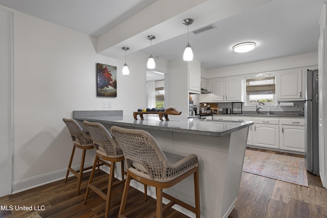 kitchen with visible vents, freestanding refrigerator, a breakfast bar, white cabinetry, and dark wood-type flooring
