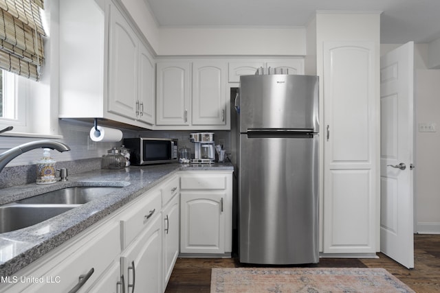 kitchen with light stone countertops, white cabinets, a sink, appliances with stainless steel finishes, and backsplash