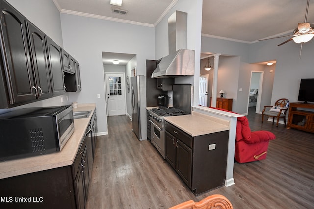 kitchen featuring ornate columns, wall chimney exhaust hood, light hardwood / wood-style flooring, crown molding, and appliances with stainless steel finishes