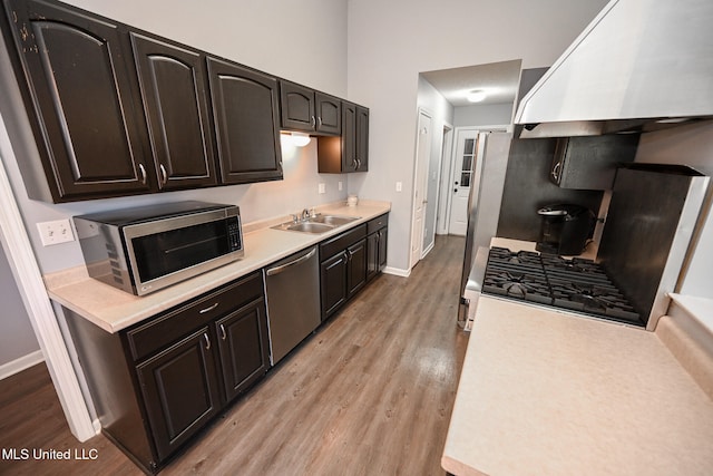 kitchen with extractor fan, stainless steel appliances, sink, dark brown cabinetry, and light wood-type flooring