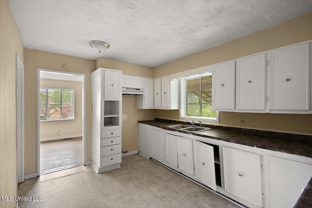 2862 Oak Forest Dr, Jackson, MS 39212 - kitchen with a sink, under cabinet range hood, white cabinets, dark countertops, and a textured ceiling