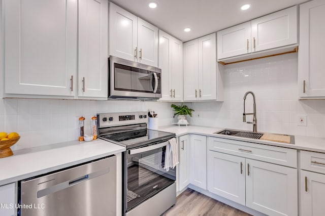 kitchen featuring white cabinets, stainless steel appliances, decorative backsplash, sink, and light wood-type flooring