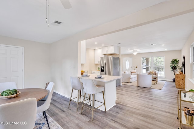 kitchen featuring ceiling fan, white cabinets, a breakfast bar, and stainless steel fridge with ice dispenser