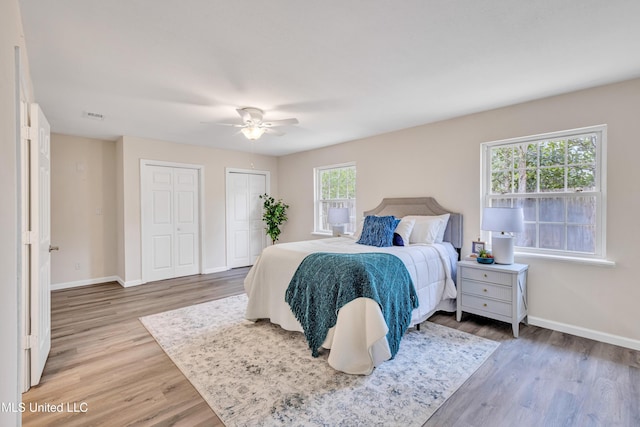 bedroom with ceiling fan, multiple closets, and hardwood / wood-style floors