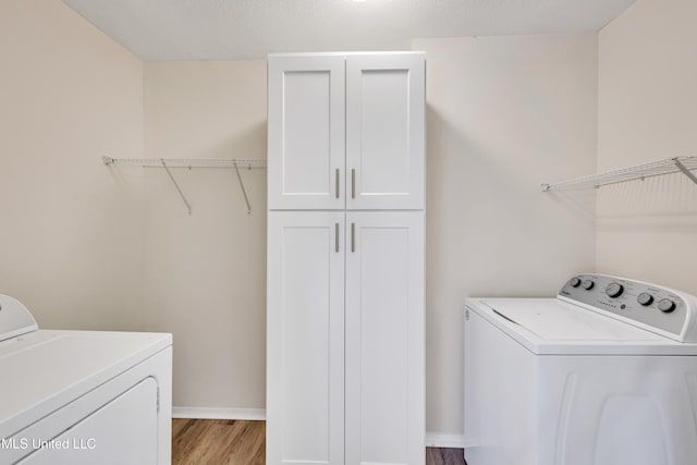 laundry area with light hardwood / wood-style floors, cabinets, a textured ceiling, and independent washer and dryer