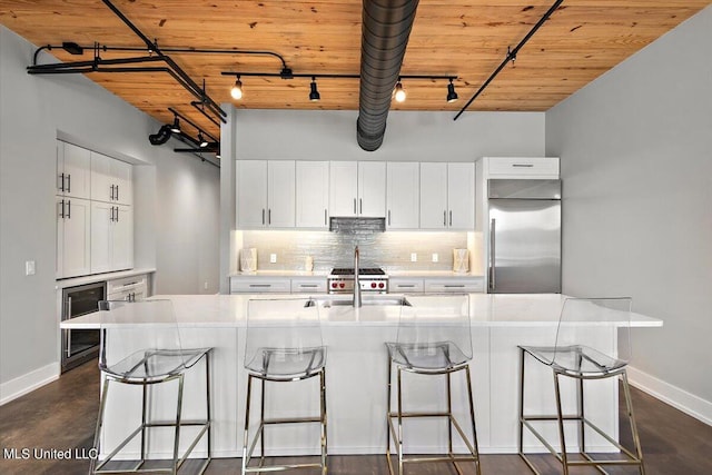 kitchen with stainless steel built in fridge, a kitchen island with sink, rail lighting, white cabinets, and sink