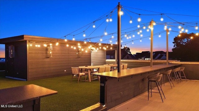 patio terrace at dusk featuring exterior bar and a lawn