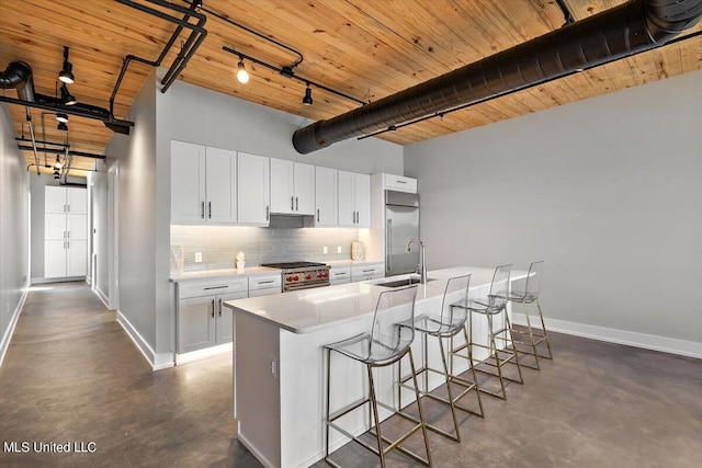 kitchen featuring high quality appliances, a kitchen bar, a kitchen island with sink, white cabinets, and sink