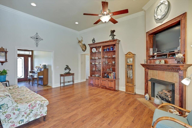 living area featuring ornamental molding, baseboards, light wood-style flooring, and a tiled fireplace