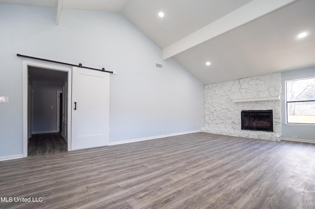 unfurnished living room with hardwood / wood-style floors, high vaulted ceiling, a stone fireplace, a barn door, and beamed ceiling