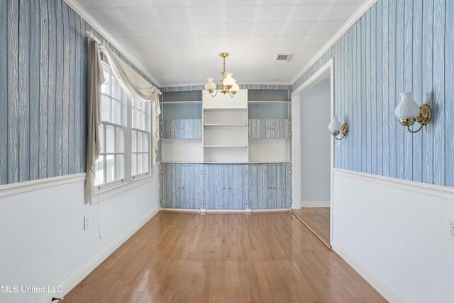 unfurnished dining area featuring hardwood / wood-style flooring, ornamental molding, and a chandelier