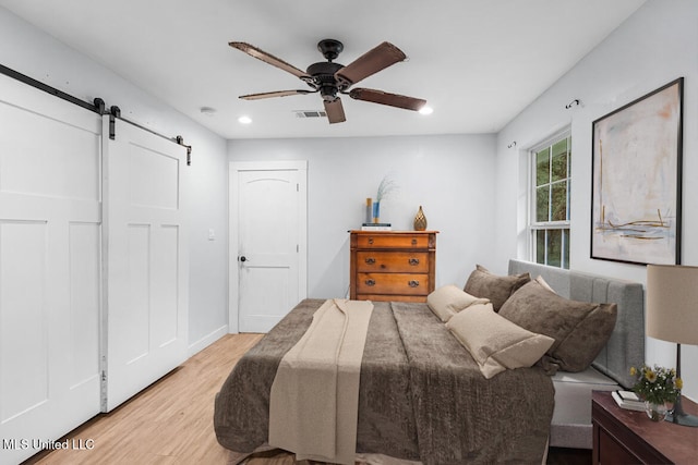 bedroom featuring a barn door, light hardwood / wood-style floors, and ceiling fan