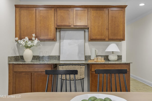 kitchen with dark stone counters, ornamental molding, and brown cabinetry