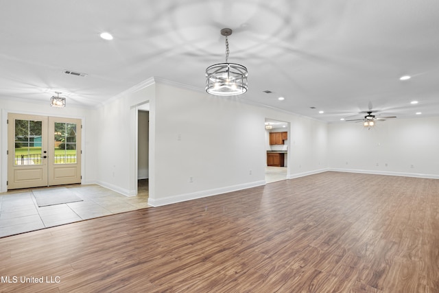 unfurnished living room with french doors, ceiling fan with notable chandelier, light hardwood / wood-style flooring, and crown molding